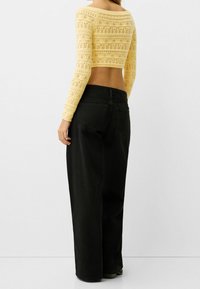 Żółty szydełkowany krótki top z długimi rękawami w połączeniu z czarnymi, szerokimi spodniami z wysokim stanem. Top ma teksturowany wzór oraz ażurowy design.
