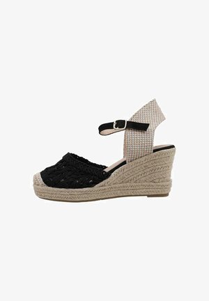 Sandale compensée en tissu noir tissé avec une semelle en jute tressé, dotée d'une sangle beige et d'une boucle réglable à la cheville.