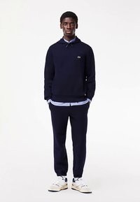 Granatowa bluza z kapturem z kieszenią kangurka, ściągaczami przy mankietach i kapturem ze ściągaczem, zestawiona z pasującymi dresami i białymi trampkami z granatowymi akcentami.