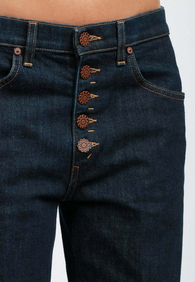 Jeans in denim scuro con un design a vita alta, cuciture arancioni visibili e chiusura decorativa con bottoni a forma di fiore.