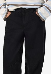 Μαύρο τζιν παν�τελόνι με ίσια γραμμή, που διαθέτει κλείσιμο με κουμπί, πλαϊνές τσέπες και ελάχιστες ραφές. Τραχιά υφή υφάσματος.