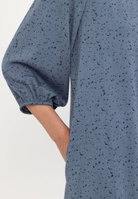 Abito blu con una vestibilità comoda, caratterizzato da maniche lunghe a sbuffo e motivi a macchie nere. Include tasche laterali e polsini elasticizzati.