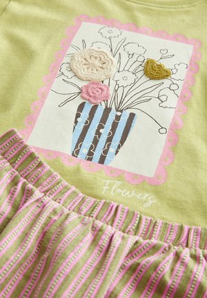 Grünes Baumwolloberteil mit floralen Druck und einer blauen gestreiften Vase. Darunter ein hellgrüner und rosa gestreifter Rock mit gerafftem Bund.