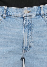 Svetlo modré džíny s vysokým pásom, vybavené kovovým zapínaním, kontrastným prešívaním a hladkým povrchom.