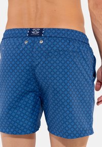 Shorts de bain bleus avec un motif géométrique en losanges, taille élastique et poches latérales. Présente un logo sur la ceinture arrière.