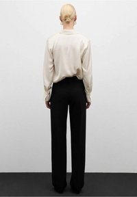 Blouse en soie crème avec col, associée à un pantalon noir ample. Texture lisse, manches longues et style minimaliste.