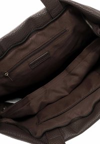 Brūna ādas tote soma ar teksturētu virsmu, tai ir rāvējslēdzēja kabata un plašas iekšējās nodalījumi, odere no gludas auduma.