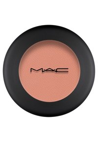 MAC blush in een ronde, matte zwarte verpakking. Het poeder heeft een zachte perzikkleur met een gestructureerd oppervlak. Logo in het midden.