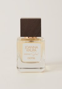 Przezroczysta szklana butelka perfum z kwadratową drewnianą zakrętką, z beżową etykietą ze złotym tekstem. Kolor zapachu to jasny żółty.