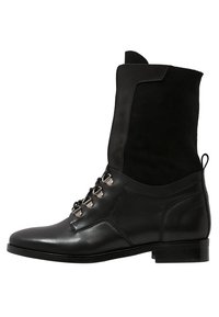 Botín negro de cuero con parte superior de ante, punta redonda, tacón plano y ojetes metálicos para los cordones. Diseño limpio con un acabado texturizado.