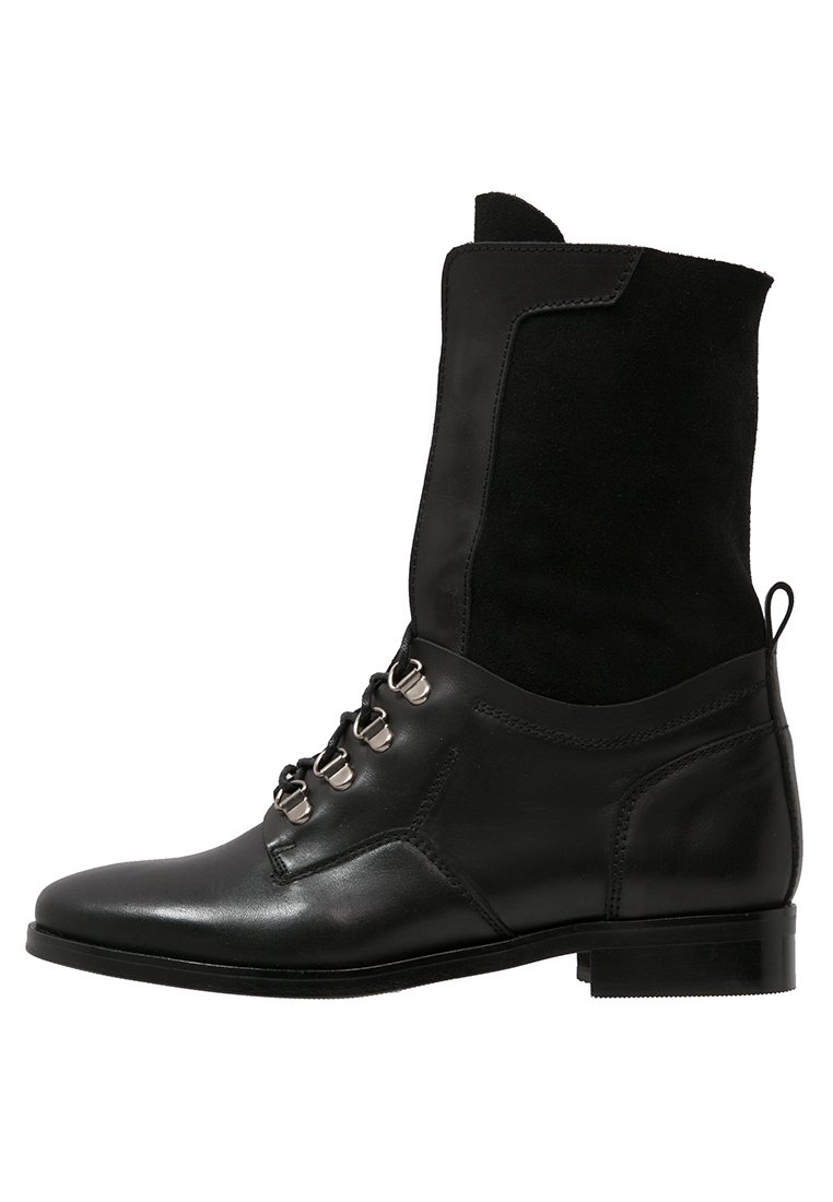 Botín negro de cuero con parte superior de ante, punta redonda, tacón plano y ojetes metálicos para los cordones. Diseño limpio con un acabado texturizado.