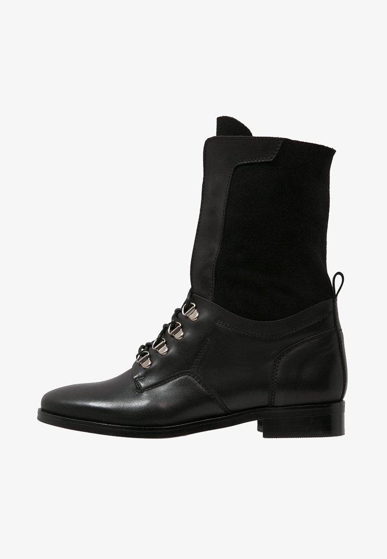 Botín negro de cuero con parte superior de ante, punta redonda, tacón plano y ojetes metálicos para los cordones. Diseño limpio con un acabado texturizado.