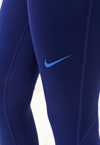 Tmavě modré sportovní legíny vyrobené z elastického materiálu, s designem postranního švu a kontrastním světle modrým logem Nike.