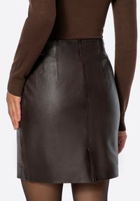 Gonna in pelle marrone con design aderente, texture liscia e spacco posteriore. Abbinata a un maglione marrone a maglia e calze nere velate.