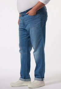 Ljust blå denimjeans med rak skärning, fem fickor och uppvikta benslut, bärs med vita träningsskor. Slät textur.