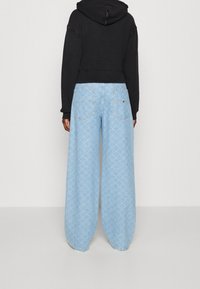 Przycięta czarna bluza z kapturem; jasnoniebieskie szerokie dżinsy z powtarzającym się geometrycznym wzorem i tylnymi kieszeniami.