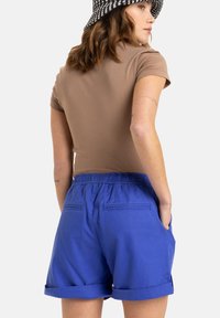 Brun, figurnära skjorta med korta ärmar, kombinerad med blå knälånga shorts med elastisk midja och uppvikta fållar.
