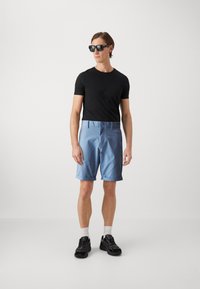 Svart t-skjorte med korte ermer som er kombinert med lyseblå shorts, med knappelukking og oppbrettet kant. Brukt med svarte sneakers og solbriller.