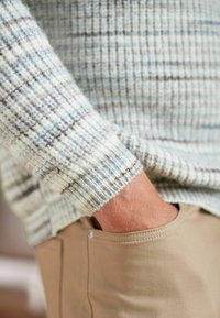 Pull en tricot bleu clair et crème avec une texture côtelée et des rayures brunes, associé à un pantalon kaki avec une poche latérale.