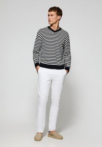 Striped navy and white sweater, v-neck, paired with white slim-fit jeans and beige espadrilles. Model stands with hands in pockets.