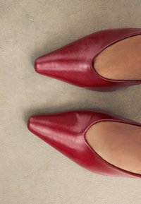 Escarpins en cuir rouge à talons hauts, à bout pointu et côtés ajourés, présentant une texture lisse et une finition brillante.