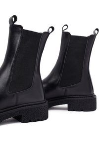 Czarne skórzane botki Chelsea z elastycznymi panelami po bokach, pętlami do zakupu oraz teksturowaną gumową podeszwą, charakteryzujące się eleganckim designem i solidną konstrukcją.