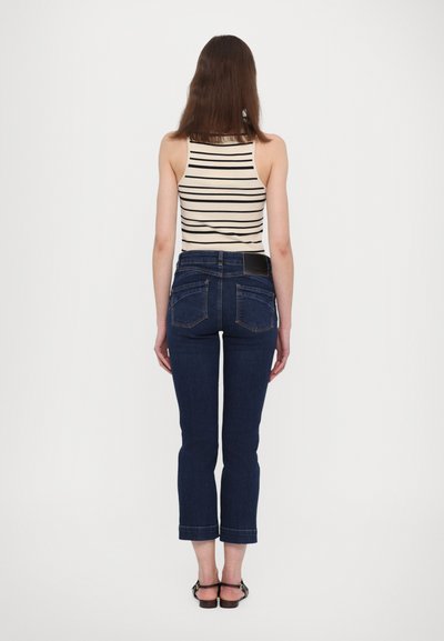 Blauwe denim jeans met een strakke pasvorm en cropped lengte, met een donkere wassing, vijf zakken en een leren label op de achterkant. Gestreepte tanktop is zichtbaar.