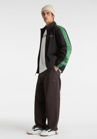 Black jacket with green checkered side panel, paired with a white shirt and brown pants. White sneakers with green accents.