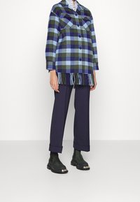 Grøn, blå og marineblå ternet oversize skjorte med to forlommer og frynset kant, kombineret med marineblå bukser og mørkegrønne ankelstøvler.