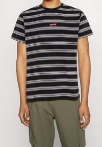 T-shirt à manches courtes à rayures noires et blanches avec un col rond, arborant un petit logo rouge Levi's sur la poitrine.
