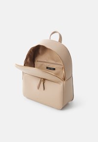 Zaino in finta pelle beige con parte superiore arrotondata, chiusura con zip, tasca frontale e fodera interna. Presenta un'etichetta con marchio e una texture sottile.