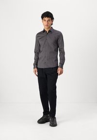 Black patterned button-up shirt with a slim fit, long sleeves, and a collar. Paired with dark trousers and athletic shoes.