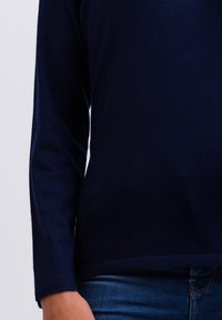 Mörkblå långärmad topp, mjukt stickat tyg, rundad nederkant, avslappnad passform, ihopparad med denimjeans, inga synliga mönster eller detaljer.