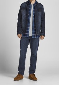 Chaqueta de denim oscura con cierre de botones, combinada con una camisa de cuadros azul y blanca, camiseta gris, jeans oscuros y zapatos de ante marrón.