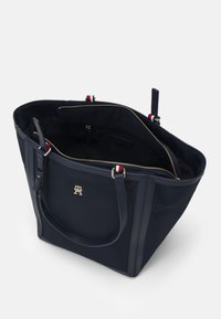 Marineblauwe tote bag met gouden accenten, voorzien van dubbele handgrepen, ritssluiting en binnenzakken. Gemaakt van duurzaam materiaal met een strakke vorm.