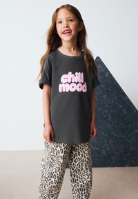 Grafikgraues T-Shirt mit dem Schriftzug „chill mood“ in fettgedruckten pinkfarbenen Buchstaben. Dazu beige Leopardenmuster-Hose. Glatte Stoffstruktur und lockere Passform.