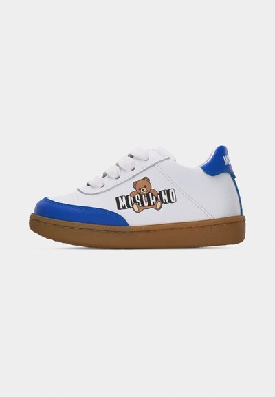 Λευκό sneaker Moschino με μπλε λεπτομέρειες στη μύτη και τη φτέρνα, καφέ σόλα, λογότυπο αρκουδάκι και λευκά κορδόνια σε απλό λευκό φόντο.