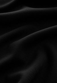 Schwarzer Stoff mit einer glatten, matten Textur, die sanfte Falten und sanfte Kurven zeigt. Keine bemerkbaren Muster oder Akzente sichtbar.