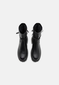 Botas de tobillo de cuero negro con un acabado suave, punta redondeada y lengüetas de agarre en el collar. Suela de goma gruesa que ofrece tracción.