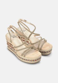 Sandales compensées avec un tissu beige et des brides dorées scintillantes. Présente une semelle tressée multicolore. Design à bout ouvert avec des brides de cheville.