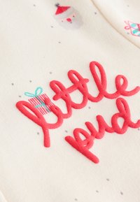 Tissu crème avec texte en relief rouge « little pud », illustré par des dessins du Père Noël et des boîtes cadeaux, ainsi que des points gris clair dispersés.