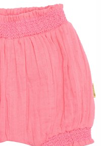 Shorts roses en tissu léger et texturé avec une ceinture smockée. Présente des plis doux et de petits points en relief pour plus de détails.
