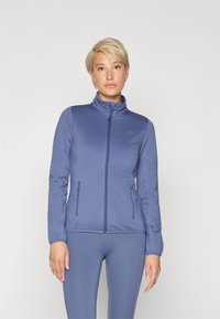 Blå zip-jakke med høy krage, laget av lett materiale, med to frontlommer med glidelås og teksturerte sidepaneler.