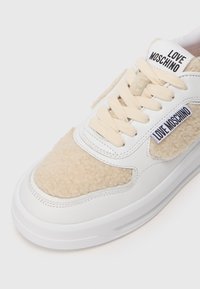 Bijele tenisice s pahuljastim bež panelima, kremastim vezicama i gumenim đonom. Na jeziku i strani se nalazi logo "LOVE MOSCHINO".