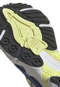 Semelle extérieure en caoutchouc noire et jaune avec des motifs texturés, dotée d'un intercalaire blanc et d'accents bleus sur le côté. Matériaux durables visibles.