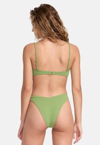 Groene bikini met fijne textuur, verstelbare bandjes en haaksluiting. Hoog uitgesneden onderkant met minimale bedekking. Achteraanzicht.