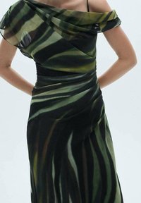 Robe noire et verte à motifs avec un décolleté asymétrique, un tissu fluide et des détails drapés sur le corsage.