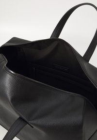 Black leather tote bag with textured surface, featuring a zip closure and a fabric-lined interior, including a zippered pocket.