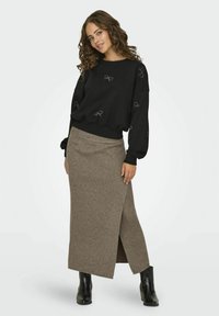 Sudadera negra con bordado de lazo y mangas abullonadas, combinada con una falda maxi marrón de canalé con una abertura lateral, llevada con botas negras.