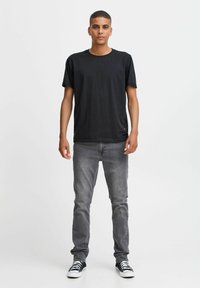 Zwarte katoenen T-shirt met korte mouwen en een ronde hals, gecombineerd met grijze jeans en zwarte sneakers met witte zolen en veters.